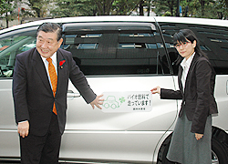 バイオ燃料を使った公用車の前に立つ　若林大臣と濱田さん