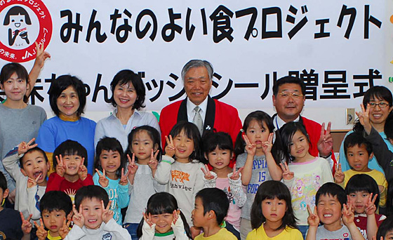 ４月５日、笑味ちゃんバッジを市内の幼稚園・保育園に贈呈した。最後列中央が萬代組合長。