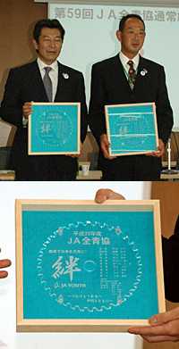 牟田氏（左）、山本毅前参与の２名には、アクリル製の草刈り羽にメッセージを刻んだ記念品が贈呈された