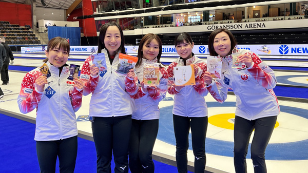 「ニッポンの食」を手に笑顔のカーリング女子日本代表（写真提供：JCA）