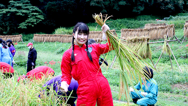 自ら手で刈り取った稲を手に笑顔の片岡未優