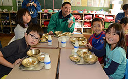 青壮年部員（中央）と一緒に給食を食べる子どもたち