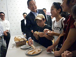 小学生とともに米粉パンを試食する山本農相。この日はグルテンを使わない米粉だけで作ったパンが提供された。