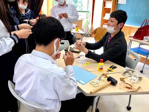 革職人の吉松さん（写真右）から革細工について学ぶ生徒たち