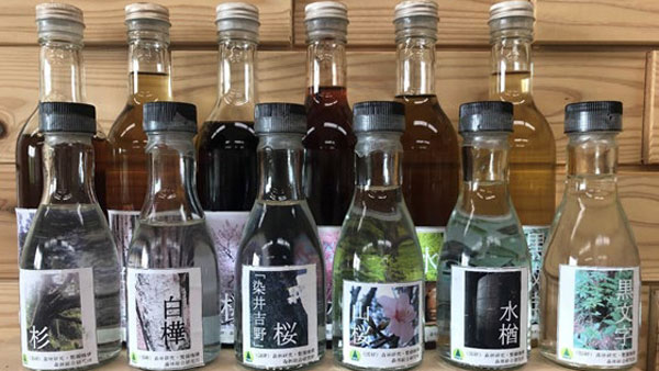 試験製造している「木の酒」。奥の6本が樹種により色の異なる醸造酒、手前の6本が蒸留酒。左からスギ、シラカンバ、ソメイヨシノ、ヤマザクラ、ミズナラ、クロモジ（提供：森林総合研究所）