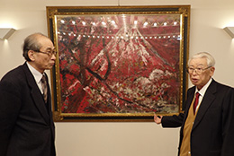 趣味で集めた絵画の前の新田会長（右）と谷口教授（平田牧場本社で。数多くの名作があり、自由に鑑賞できる）