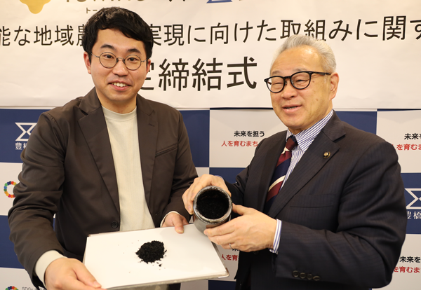 協定締結式で「宙炭」を手にする豊橋市の浅井由崇市長（右）ろTOWINGの西田宏平代表取締役CEO